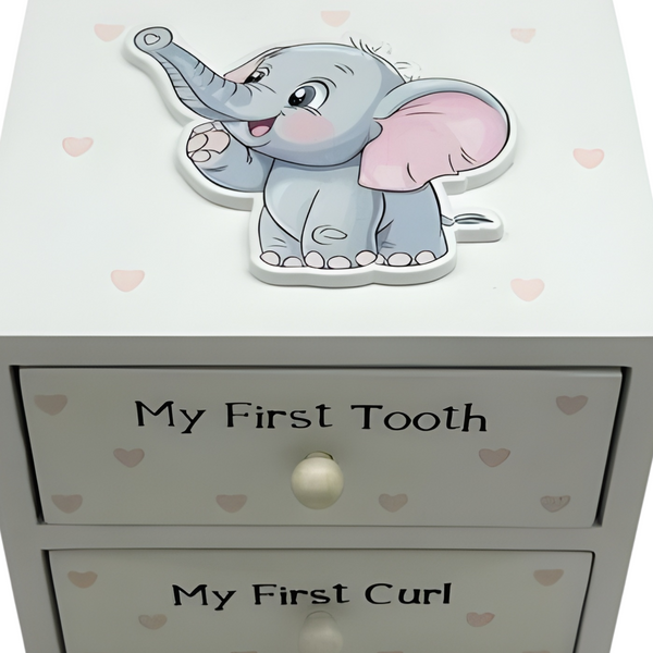 A baby keepsake box with two drawers labelled 'My First Tooth' and 'My First Curl', featuring a cute grey 3D elephant decoration on top and small pink hearts printed on the front. PALM GIFTS