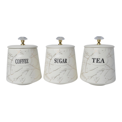 Three white ceramic kitchen canisters with gold marble design and gold handles, each labelled with different contents: coffee, sugar, and tea.
